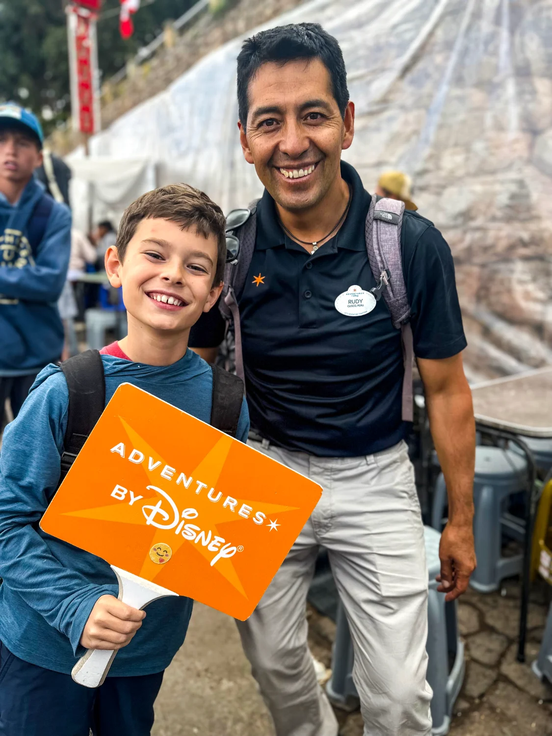 A boy and an Adventures by Disney guide hold a trip sign