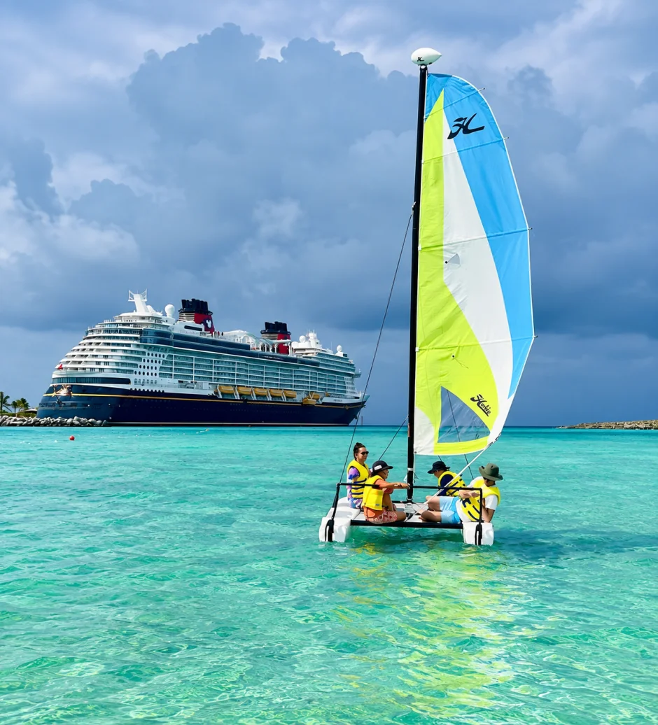 A family enjoys a catamaran excursion with a Disney cruise ship in the background